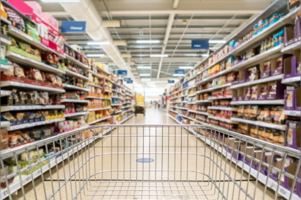 Ein Einkaufswagen fährt an den Supermarktregalen mit Hersteller- und Handelsmarken vorbei