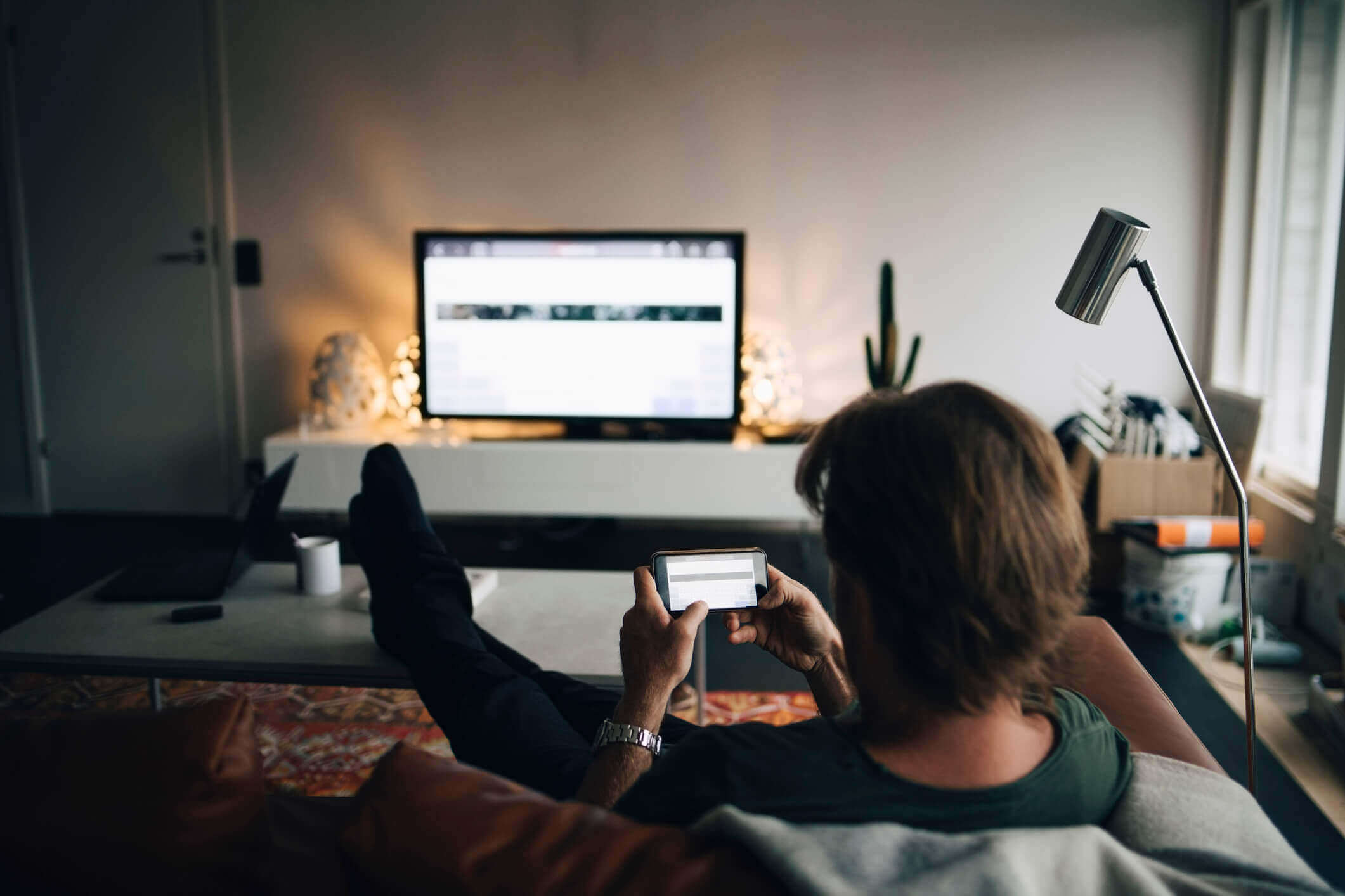 Mann-sitzt-mit-Smartphone-auf-der-Couch-und-schaut-Fernsehen