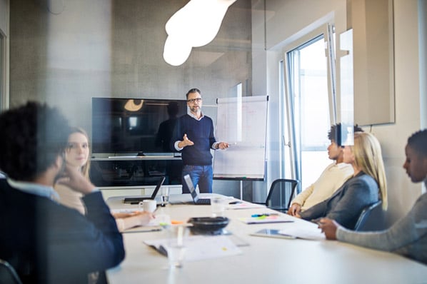 Mitarbeiter spricht ueber Dienstleistungsmarketing vor Team in Meeting-Raum