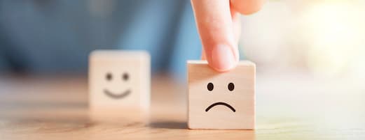 taxa de cancelamento (ou churn) representada em imagem com dois dados de madeira, um com o desenho de um rosto feliz, ao fundo e um com o desenho de um rosto triste, em destaque e focado