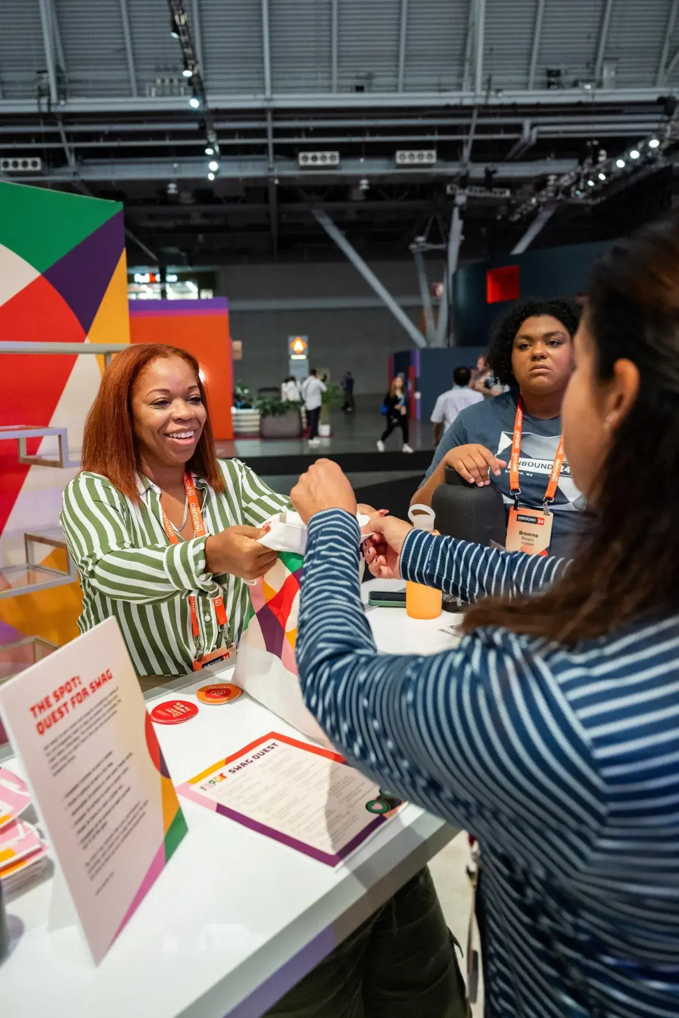 A woman working at The Spots INBOUND booth hands swag to a participant.