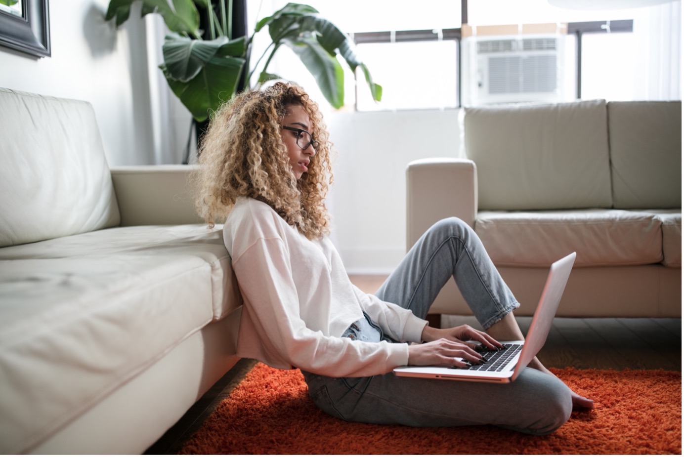 femme sur son PC assise par terre dos à son canapé