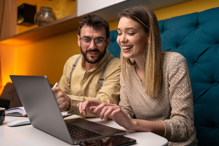 dois funcionários do time de marketing conversando a respeito da estratégia de marketing para redes sociais - os dois estão sentados em frente a um computador, revisando o conteúdo