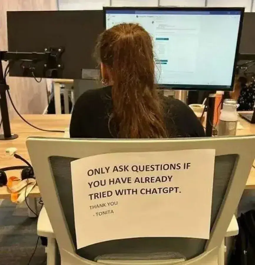 what jobs will ai replace? photo of woman at desk with a sign on her chair saying only ask questions if you have already tried with chatgpt.